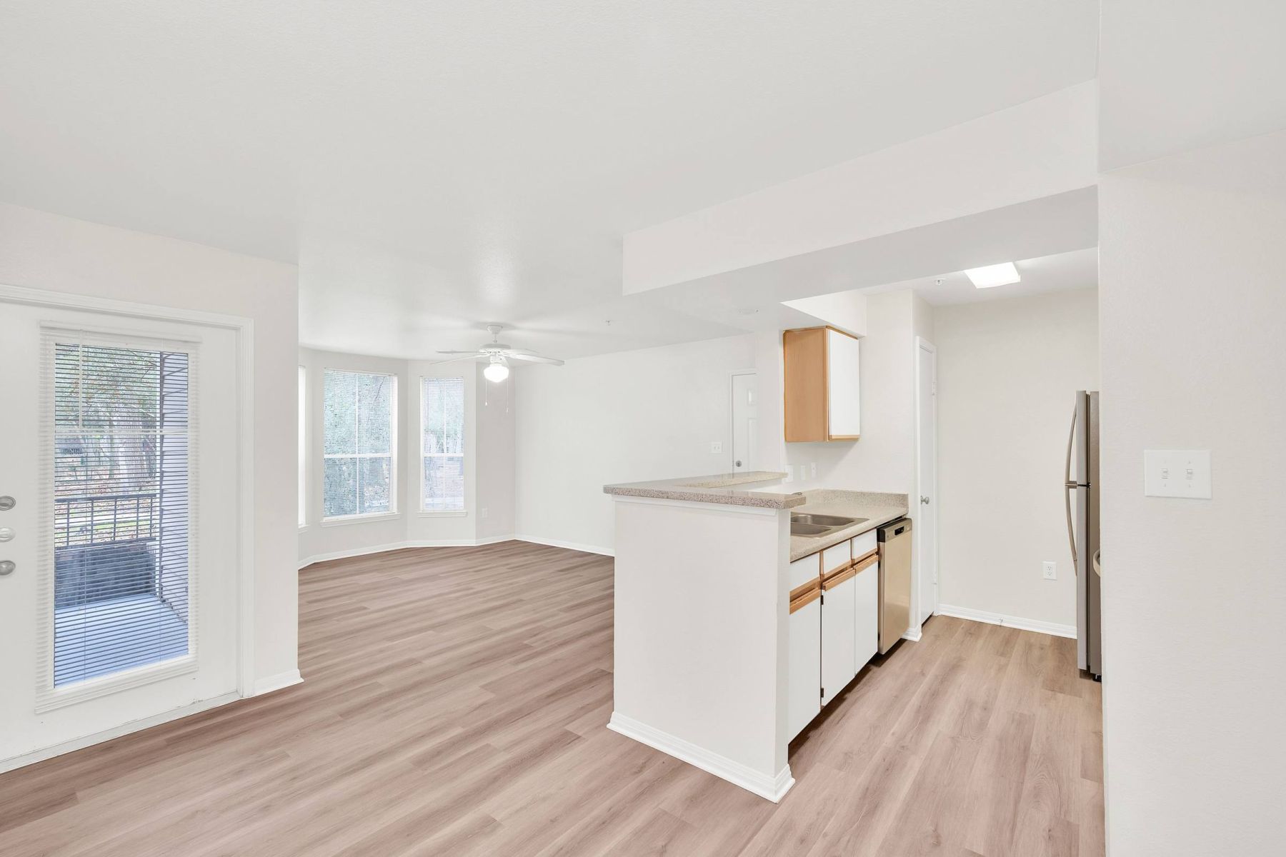 Empty room with wood floors, ceiling fan, and sliding glass door leading to a patio with vertical blinds at Apex West Midown.